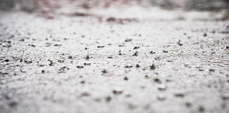 På ojämn blanksvart asfalt studsar regndroppar.